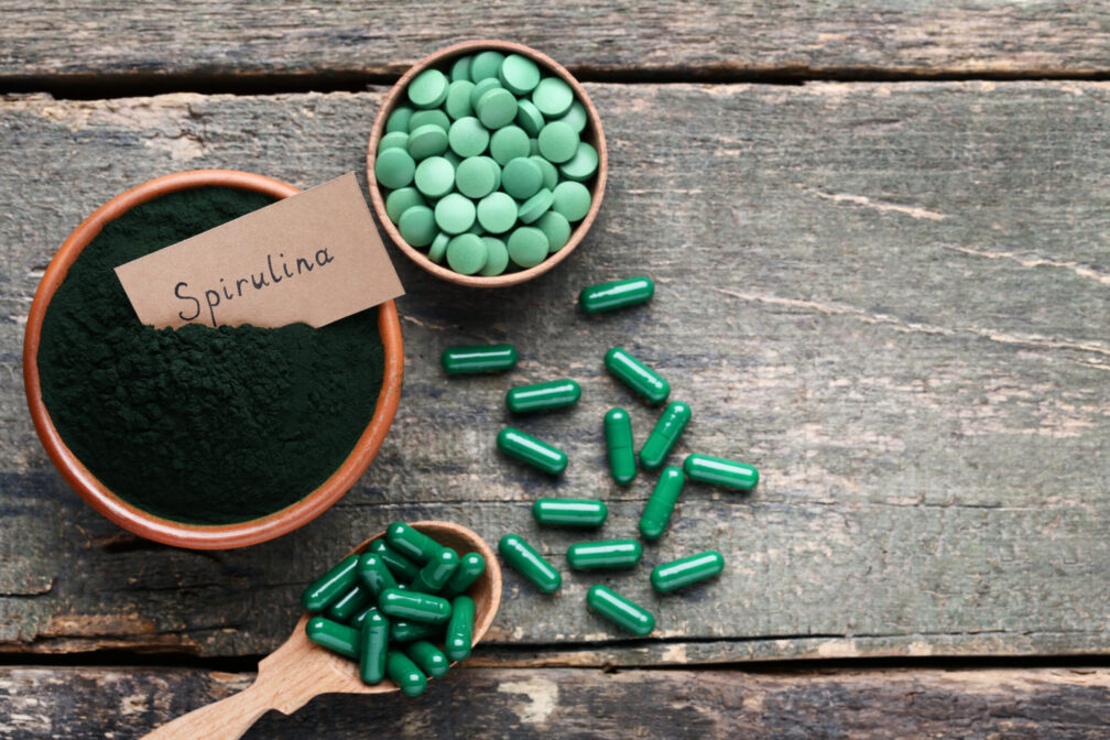 Alga spirulina a cosa serve: capsule verdi, polvere nera in ciotola e dosatori, presentazione di integratori alimentari.